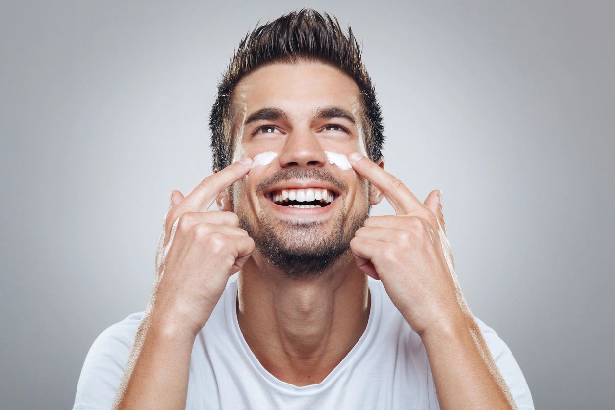 A man putting cream on his face and smiling.